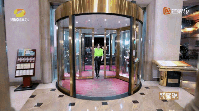 a man in a green shirt is walking through a revolving glass door with a sign that says tv on it