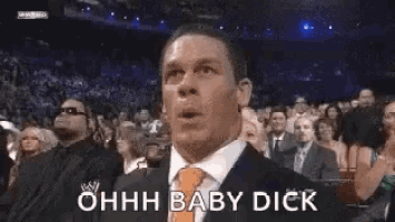 a man in a suit and tie is making a funny face while sitting in front of a crowd of people .