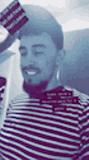 a man with a beard is wearing a striped shirt and holding a flag in his hand .