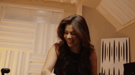 a woman in a black tank top is smiling in a room with a striped wall