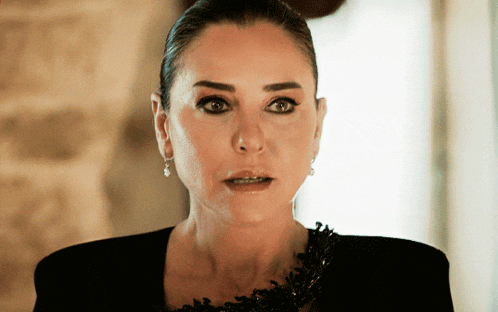 a woman wearing a black jacket and earrings looks at the camera with a surprised look on her face