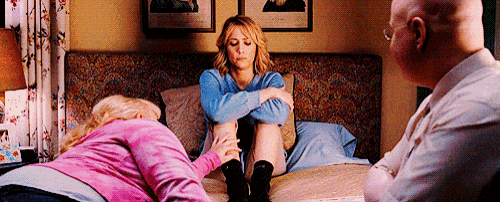 a woman is sitting on a bed with her legs crossed while a man and a woman sit on the bed .