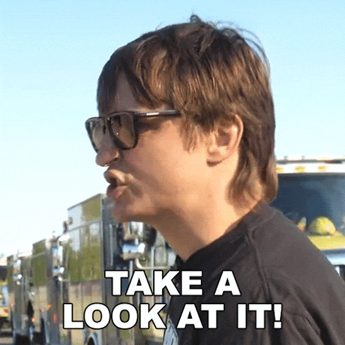 a man wearing sunglasses says " take a look at it " in front of a fire truck