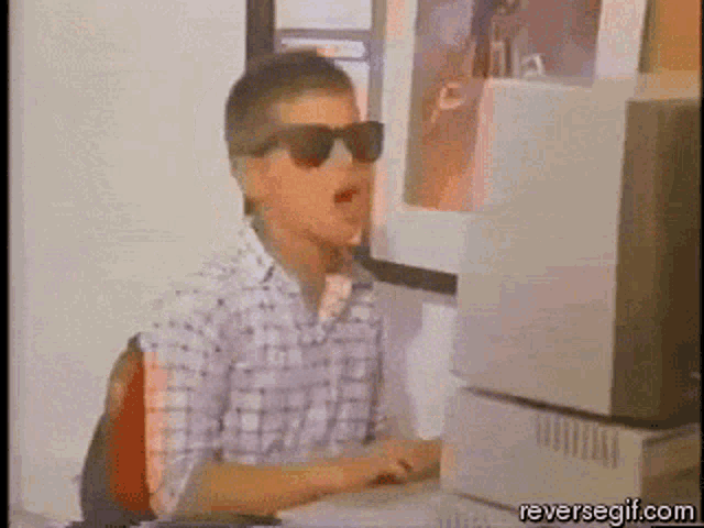 a man wearing sunglasses is sitting at a computer desk