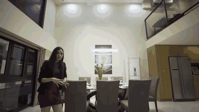a woman in a red dress stands in front of a dining room table and chairs