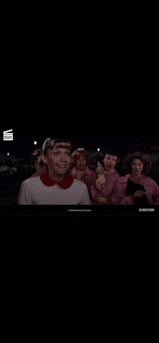 a woman in a white shirt and red collar is standing in front of a group of girls in pink jackets .