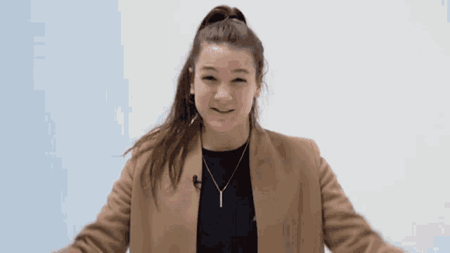 a woman wearing a tan jacket and a necklace is making a funny face .