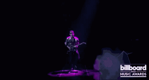 a man is playing a guitar in front of a purple light .