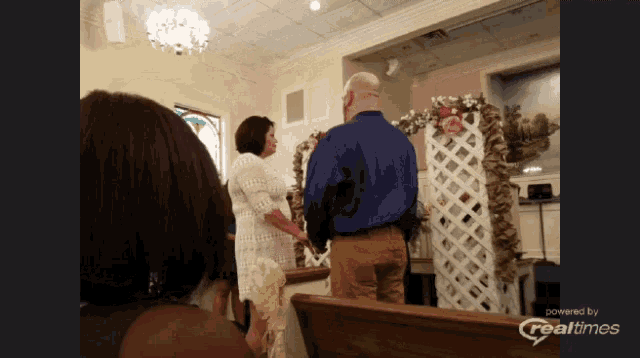 a man and woman are getting married in a church with a realtimes logo on the bottom right