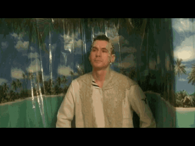 a man in a white shirt is standing in front of a curtain with palm trees on it
