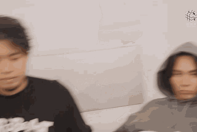 two men are sitting next to each other on a couch . one of the men is wearing a hoodie .