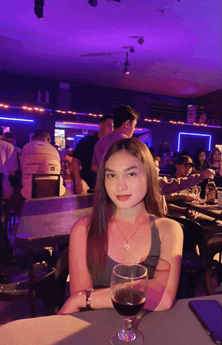 a woman sits at a table with a glass of wine in front of her
