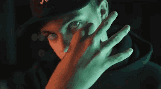 a man in a hat is covering his face with his hands .