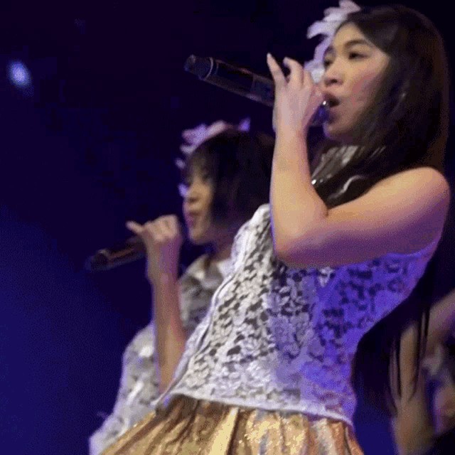 two women singing into microphones on a stage