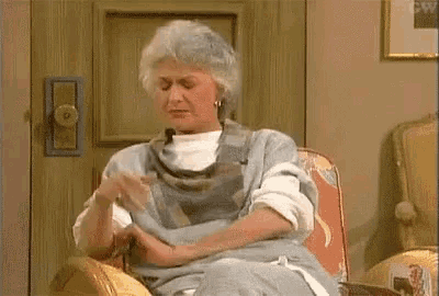 an elderly woman is sitting in a chair with her hands on her lap .