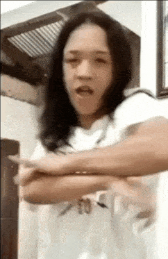 a woman with long black hair is standing with her arms crossed and making a funny face .