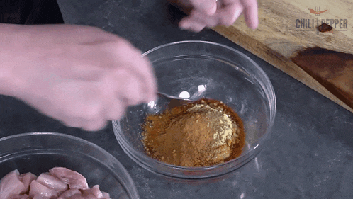 a person mixing spices in a glass bowl with a chilli pepper logo in the corner