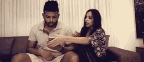 a man and a woman are sitting on a couch looking at a cell phone together .