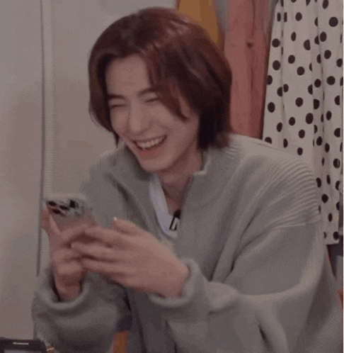 a young man with long hair is laughing while looking at his phone .