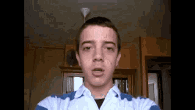 a young man in a blue and white striped shirt is making a face