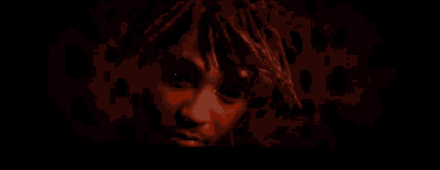 a close up of a person 's face with dreadlocks in a dark room with a red background .