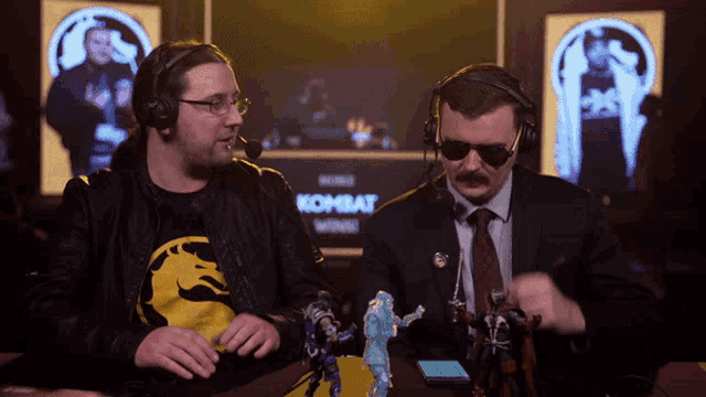 two men wearing headphones are sitting in front of a sign that says kombat wings