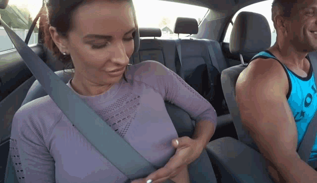a woman is adjusting her seat belt while sitting in a car with a man