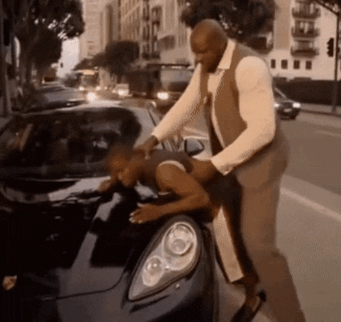 a man in a suit is putting a woman on the back of a car