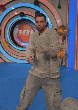 a man in a grey sweater is standing in front of a colorful circular wall
