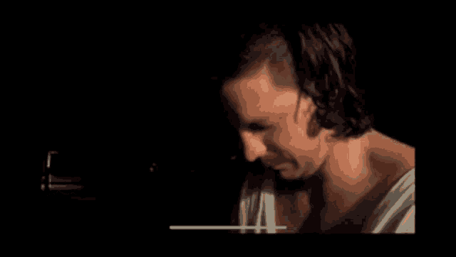 a man with long hair and a mustache is looking down in a dark room