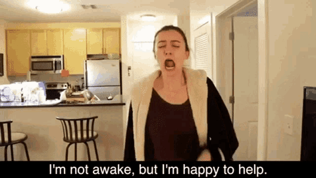 a woman yawning in a kitchen with the words i 'm not awake but i 'm happy to help behind her