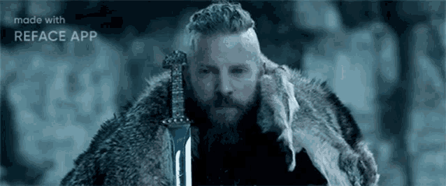 a man with a beard is holding a sword in his hand in the snow .