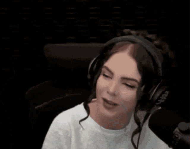 a woman wearing headphones and a white shirt is sitting in front of a microphone .