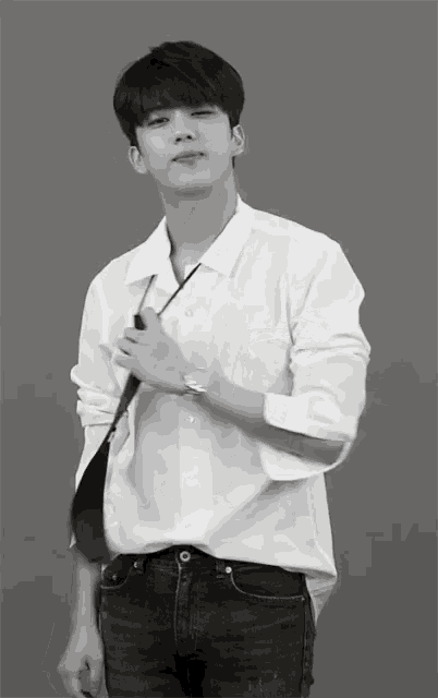 a young man in a white shirt and black jeans is adjusting his tie