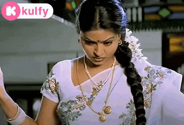a woman in a white saree with a braid is standing in front of a window .