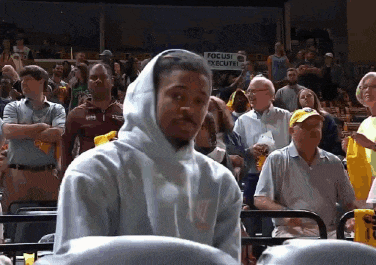 a man wearing a hooded sweatshirt is sitting in a stadium with a sign that says focus on executing