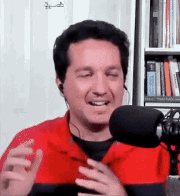 a man wearing ear buds and a red shirt is smiling in front of a microphone