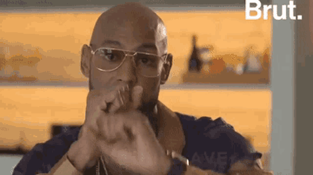 a bald man wearing glasses and a purple shirt is sitting in front of a wall .