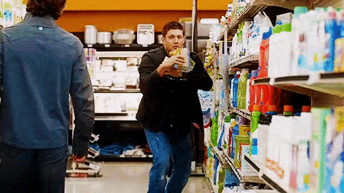 a man in a black jacket is holding a glass of water in a grocery store aisle