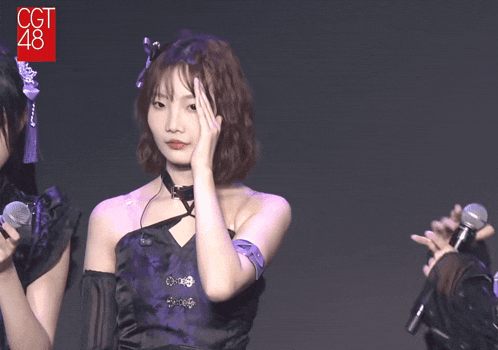 a girl in a purple dress holds her hand to her face in front of a microphone that says cgt 48