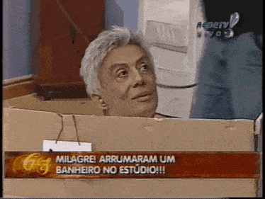 a man is sitting in a cardboard box with the words millagre arrrumaram um banheiro no estudio