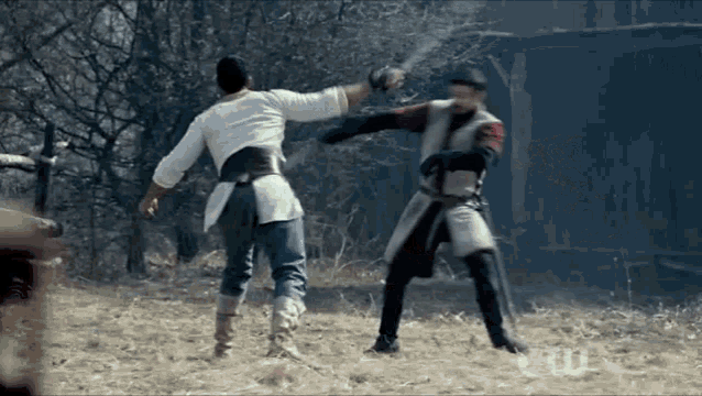 two men are fighting with swords in a field and one is wearing a white shirt .