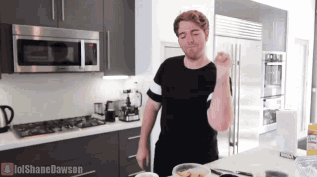 a man in a black shirt is standing in a kitchen with lolshanedawson written on the counter