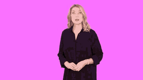 a woman in a black dress is making a funny face with her hands outstretched on a pink background .