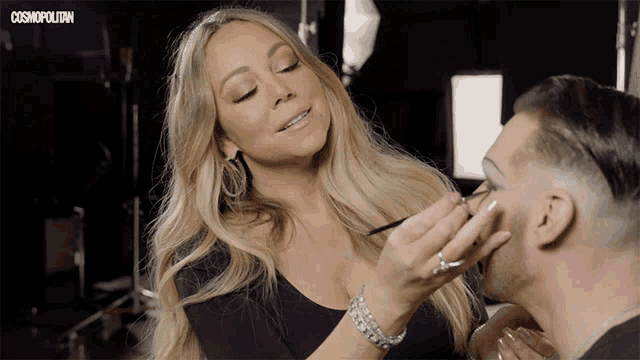 a woman is applying makeup to a man 's face with a cosmopolitan logo behind her