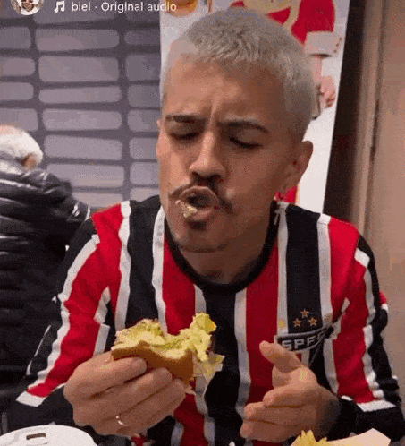 a man in a red and black striped shirt is eating a sandwich .