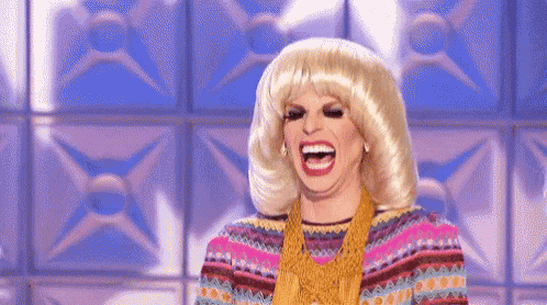 a woman wearing a wig and a colorful sweater is laughing .