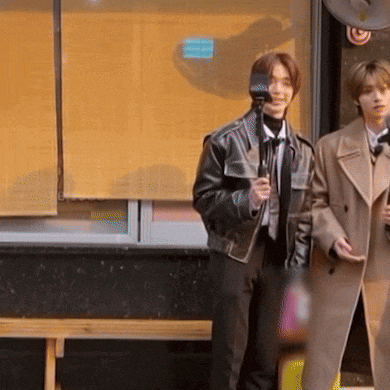 a man in a leather jacket holds a microphone while standing next to another man