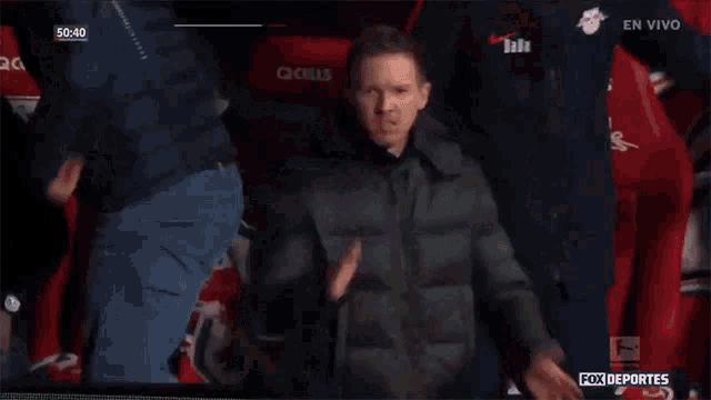 a man in a black jacket stands in front of a red qcells seat