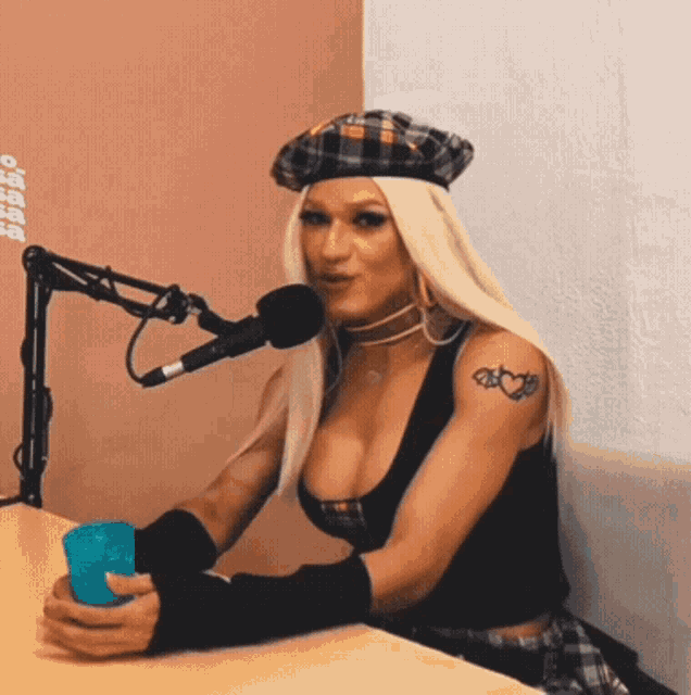a woman with a tattoo on her arm is sitting in front of a microphone holding a cup